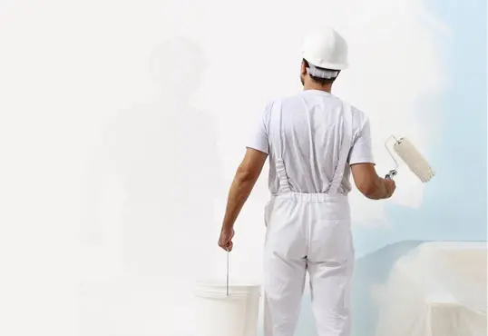 A man in white overalls and hard hat painting the wall.