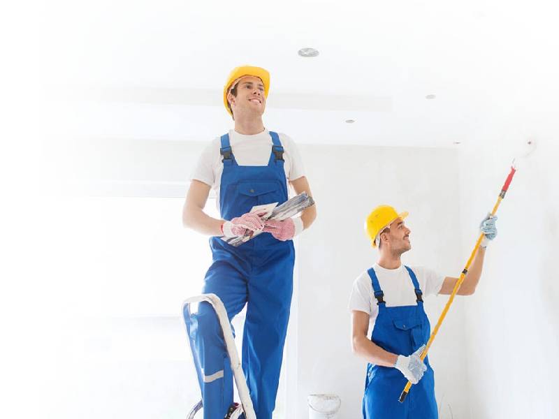Two men in blue overalls and hard hats holding tools.