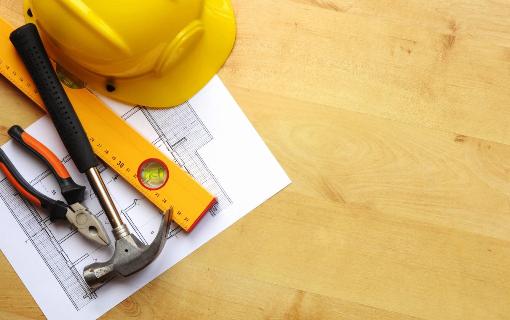 A yellow hard hat, hammer and wrench on top of construction plans.