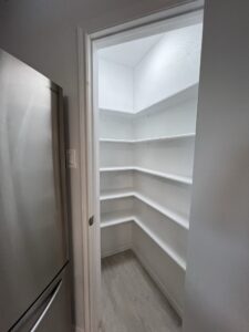 A white pantry with shelves and a refrigerator.